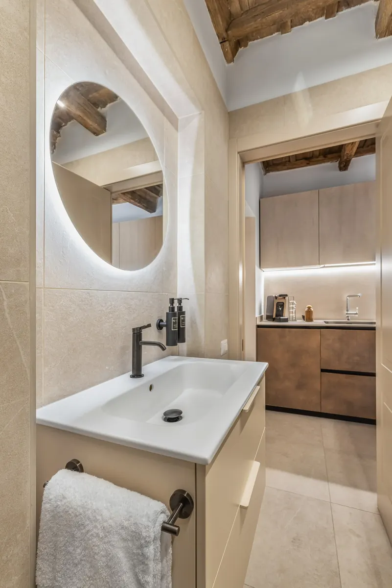 Lavabo con specchio tondo retroilluminato e scorcio dell'angolo cucina