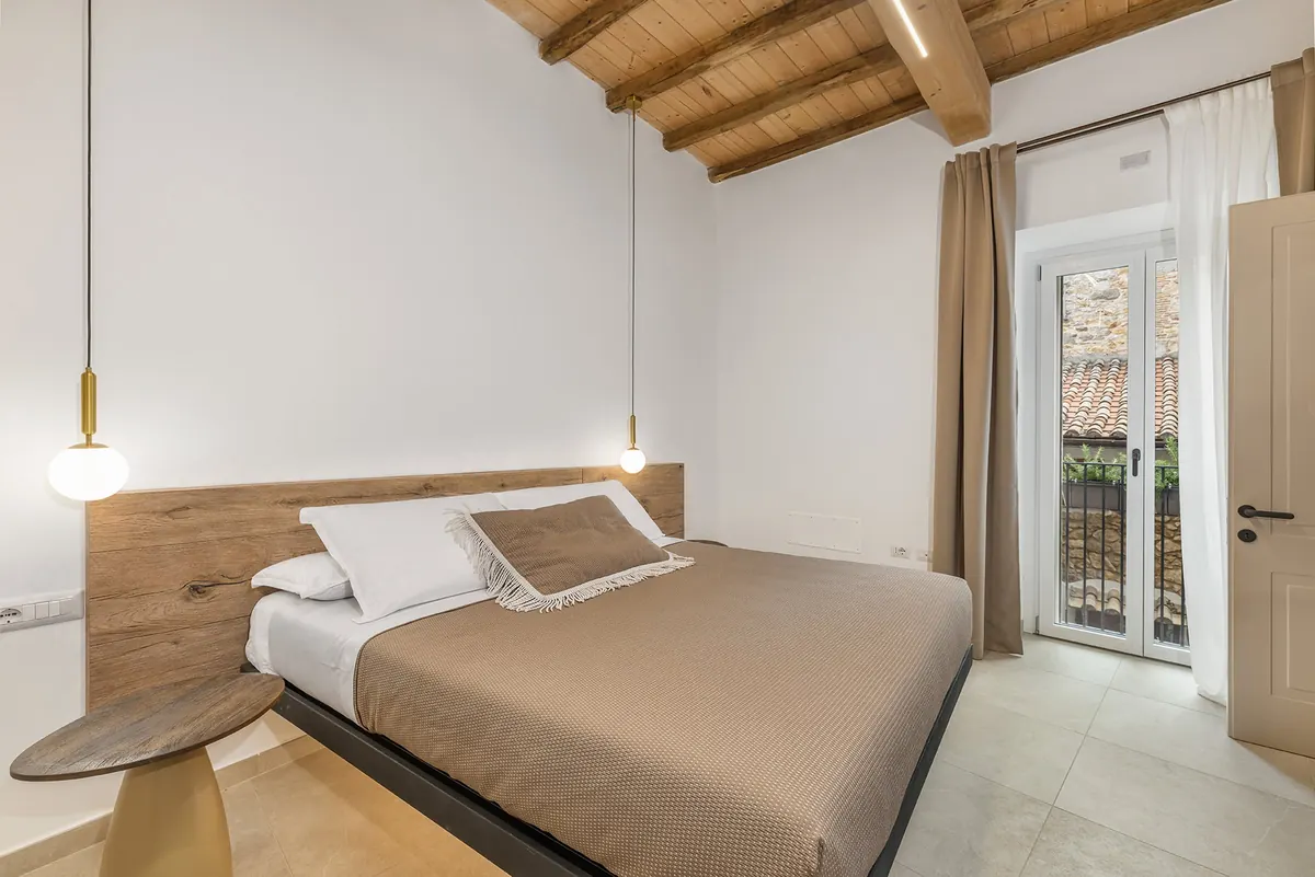 Letto e porta-finestra con balcone affacciato sui tetti di Tolfa